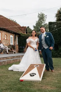 Newlyweds beside a cornhole garden game at their wedding